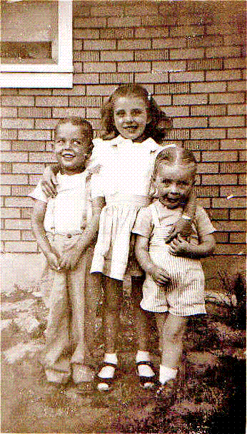 From left to right, my brother, John, sister, Barbara, and me sitting on foundation of our house on North Avenue in Fruitvale, Colorado